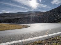 a curved asphalt road with hills in the background on an overcast day with sun shining