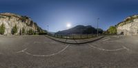 a panorama lens in use for the photograph of a view of mountains and the sun in a half empty parking lot