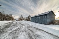 a barn sitting next to a parking lot covered in snow and snow drifters on the street