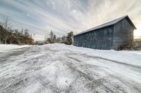 a barn sitting next to a parking lot covered in snow and snow drifters on the street