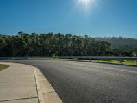 the sun is shining in the blue sky above an empty asphalt street, with trees on either side and a paved roadway in the distance