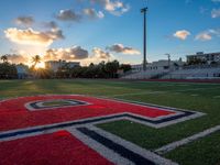 the sun setting behind the letters of the school on the field, with the sports stadium in the background