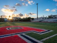 the sun setting behind the letters of the school on the field, with the sports stadium in the background