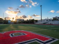 the sun setting behind the letters of the school on the field, with the sports stadium in the background