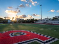 the sun setting behind the letters of the school on the field, with the sports stadium in the background