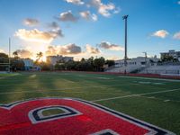 the sun setting behind the letters of the school on the field, with the sports stadium in the background