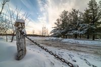 there is snow on the ground and some trees near the road in winter time with chains in front of it