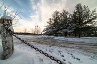 there is snow on the ground and some trees near the road in winter time with chains in front of it