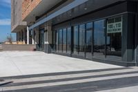 two people walking down the sidewalk next to a building with large windows on either side of it and a parking meter in front of them