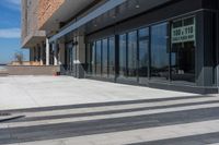 two people walking down the sidewalk next to a building with large windows on either side of it and a parking meter in front of them