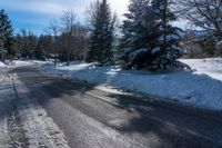 snow - covered roadway with evergreens near an intersection on a sunny winter day with the sun shining