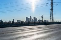 the sun is shining down over a highway with city buildings in the distance and blue skies