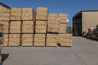 stacks of cardboard boxes next to a building near a truck full of pallets of wood