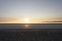 a sunrise on an empty asphalt surface with one skateboarder on the pavement looking down at the distance