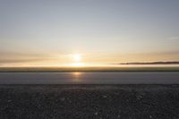 a sunrise on an empty asphalt surface with one skateboarder on the pavement looking down at the distance