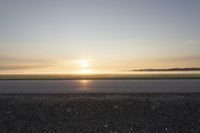 a sunrise on an empty asphalt surface with one skateboarder on the pavement looking down at the distance