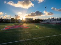 an empty field with a football stadium with seats on each side and the sun setting behind it