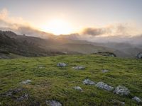 the sun is setting on top of the green mountainside with mossy rocks and grass