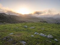 the sun is setting on top of the green mountainside with mossy rocks and grass