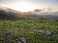 the sun is setting on top of the green mountainside with mossy rocks and grass