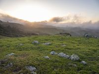 the sun is setting on top of the green mountainside with mossy rocks and grass