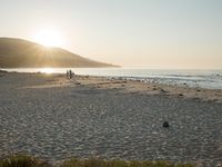 the sun is rising over the water, and the people on the beach are walking toward the shore
