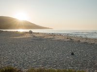 the sun is rising over the water, and the people on the beach are walking toward the shore