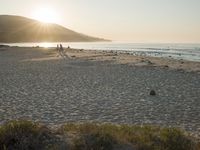 the sun is rising over the water, and the people on the beach are walking toward the shore