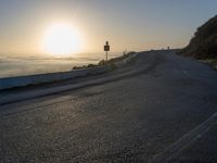 the sun is rising over the ocean on a road with a couple of bikers