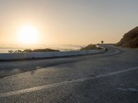 the sun is rising over the ocean on a road with a couple of bikers