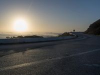 the sun is rising over the ocean on a road with a couple of bikers