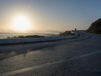 the sun is rising over the ocean on a road with a couple of bikers
