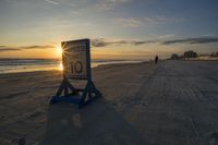 a speed limit sign sits on the sand at sunset near the ocean edge while the sun rises