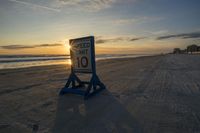 a speed limit sign sits on the sand at sunset near the ocean edge while the sun rises