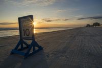 a speed limit sign sits on the sand at sunset near the ocean edge while the sun rises