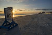 a speed limit sign sits on the sand at sunset near the ocean edge while the sun rises