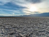 the sun is setting over a field full of white sand and mountains in the distance