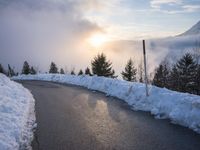 the sun is rising over a long, empty road and mountain range covered in snow