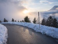 the sun is rising over a long, empty road and mountain range covered in snow