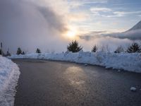 the sun is rising over a long, empty road and mountain range covered in snow