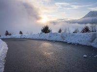 the sun is rising over a long, empty road and mountain range covered in snow