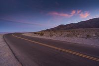 this is an image of a lonely road in the desert at sunset time with purple and pink clouds