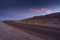 this is an image of a lonely road in the desert at sunset time with purple and pink clouds