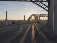 a train moving on a bridge at sunrise over the street and cars driving on the road