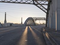 a train moving on a bridge at sunrise over the street and cars driving on the road