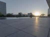 a fountain in the middle of a public park at sunrise time with the sun setting over buildings