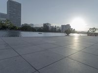 a fountain in the middle of a public park at sunrise time with the sun setting over buildings