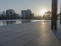 a fountain in the middle of a public park at sunrise time with the sun setting over buildings