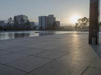 a fountain in the middle of a public park at sunrise time with the sun setting over buildings