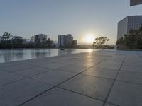 a fountain in the middle of a public park at sunrise time with the sun setting over buildings